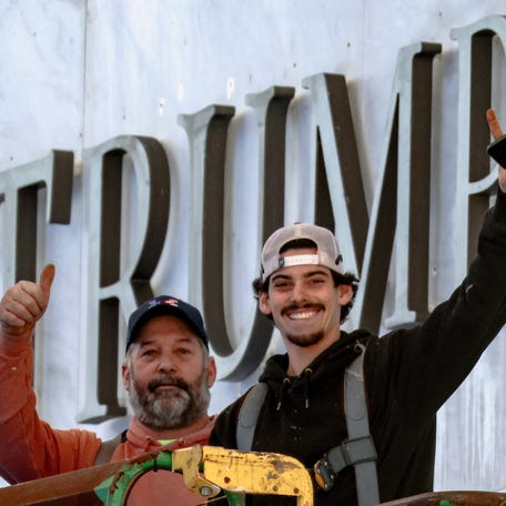 Workers react to journalists watching the installation of President Donald Trump's name on the facade of the John F. Kennedy Center for the Performing Arts in Washington, DC, on Dec. 19, 2025. The sign on the building now reads 