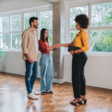 A real estate agent shaking hands with a smiling couple while showing them an empty apartment during a property visit. Concept of buying, renting, or real estate negotiation