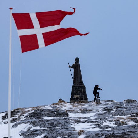 A man walks as a Danish flag flutters next to a statue of Hans Egede, a Danish-Norwegian missionary, in Nuuk, Greenland, on March 9, 2025.