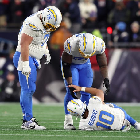 Justin Herbert #10 of the Los Angeles Chargers is helped up by teammates after a play against the New England Patriots during the fourth quarter of the AFC Wild Card Playoff game at Gillette Stadium on January 11, 2026 in Foxborough, Massachusetts.