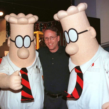 Scott Adams, the creator of "Dilbert," the cartoon character that lampoons the absurdities of corporate life, poses with two "Dilbert" characters at a party in 1999 in Pasadena, California.