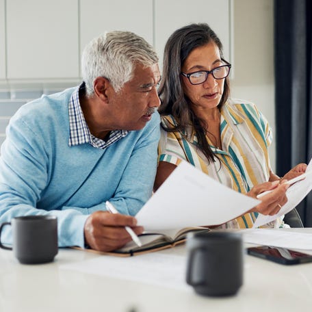 An older couple is sitting at their kitchen table reviewing financial documents.