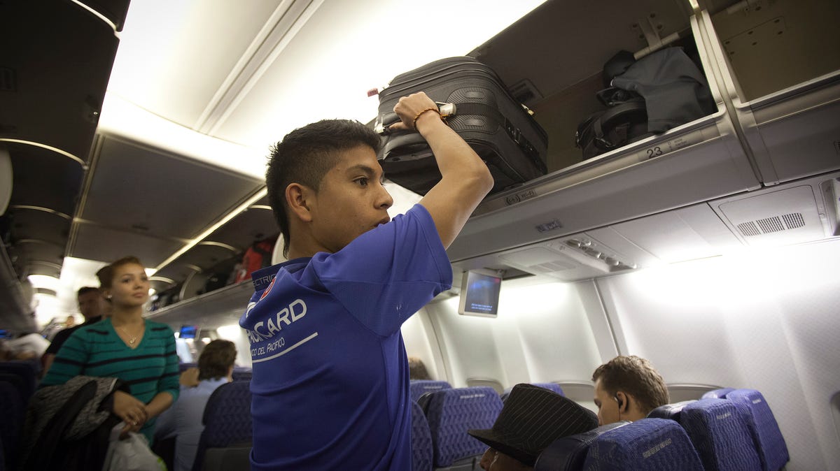 A passenger places his luggage into the overhead bin before an American Airlines flight from Miami to New York December 10, 2013.