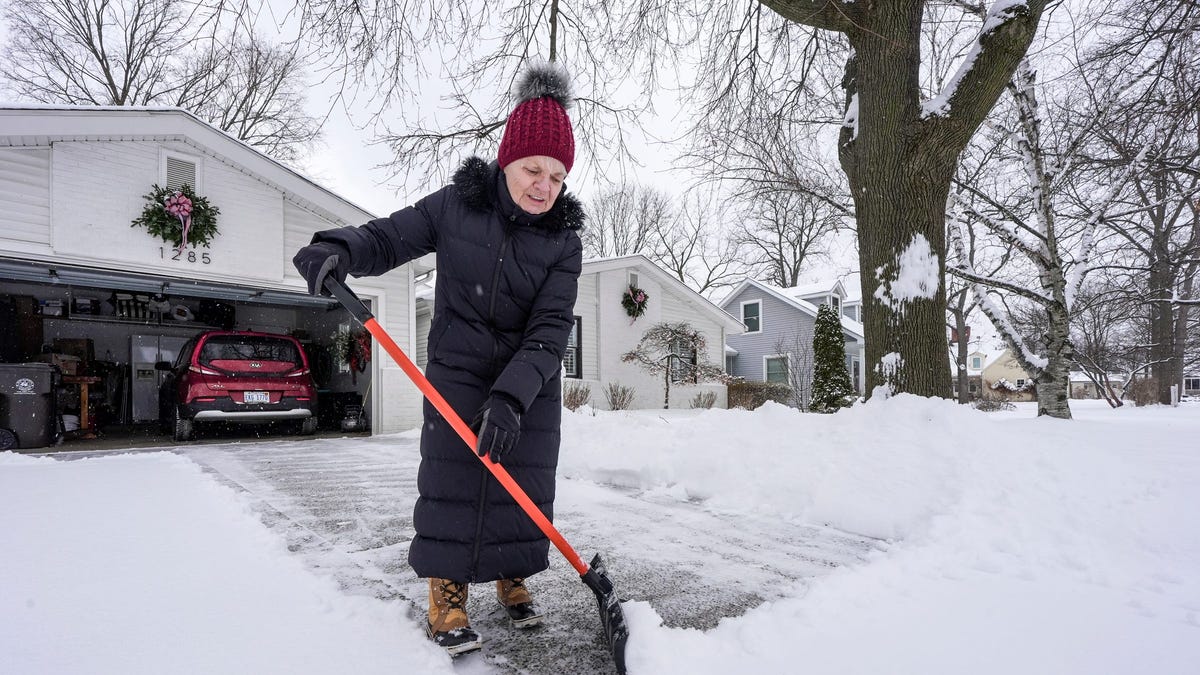 Caol Goode, 78, of Plymouth, Michigan, clears the fresh snow from the driveway of her 1965 bungalow on Wednesday, Jan. 21, 2026.