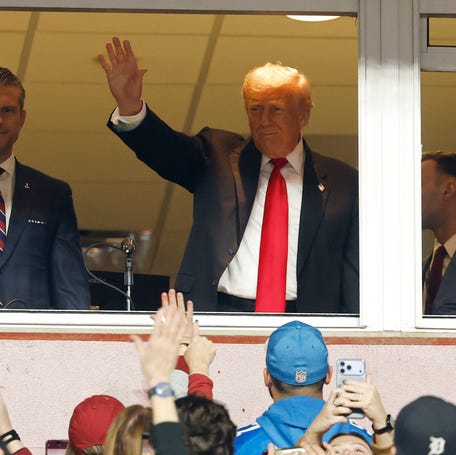 Nov 9, 2025; Landover, Maryland, USA; President Donald Trump waves to fans while standing next to U.S. Secretary of War Pete Hegseth (L) after swearing in a new group of U.S. military recruits during halftime of the game between the Lions and Commanders.