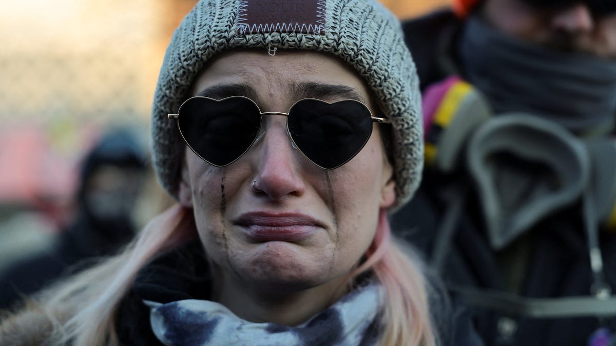 A woman cries as people gather around a makeshift memorial at the site where a man identified as Alex Pretti was fatally shot by federal agents trying to detain him, in Minneapolis, Minnesota, U.S., January 24, 2026.