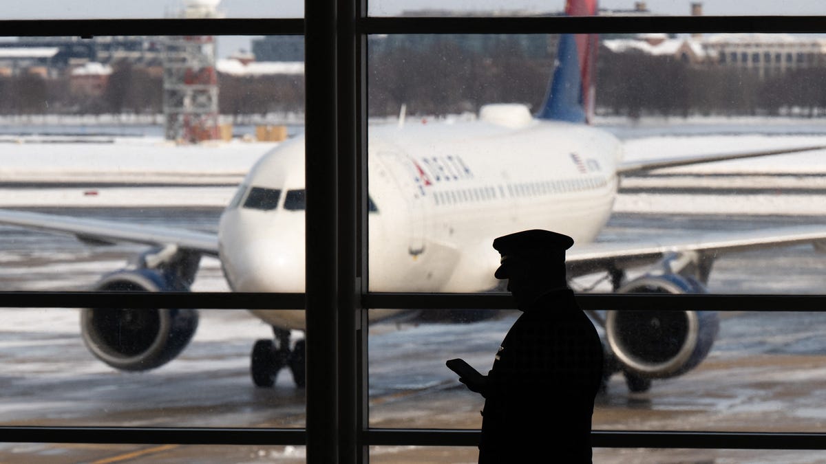 A pilot walks past a Delta Air Lines airplane as flights are delayed and cancelled following a significant winter storm at Ronald Reagan Washington National Airport in Arlington, Va., Jan. 26, 2026.