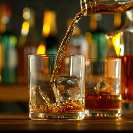 Close-up of pouring whiskey or rum on the bar, dark toned background