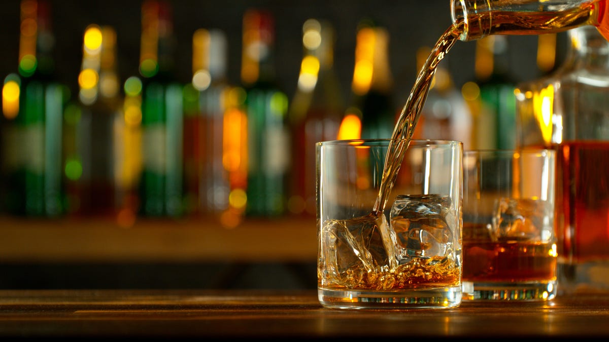 Close-up of pouring whiskey or rum on the bar, dark toned background
