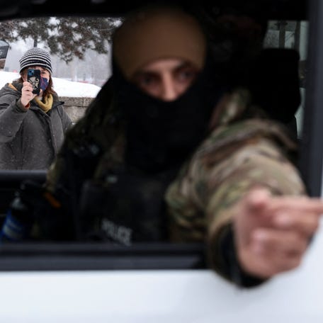 A person holds a phone as a federal agent looks on and points from inside a vehicle, as immigration enforcement continues after a U.S. Immigration and Customs Enforcement (ICE) agent fatally shot Renee Nicole Good on January 7, in Minneapolis, Minnesota.