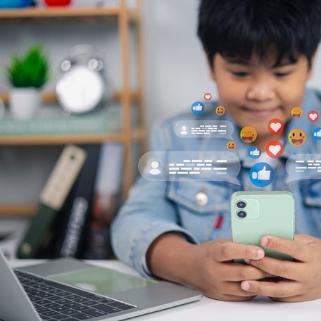Asian boy using smartphone with social media reaction icons, chatting and online communication concept. Digital lifestyle, internet technology, children using mobile phone.