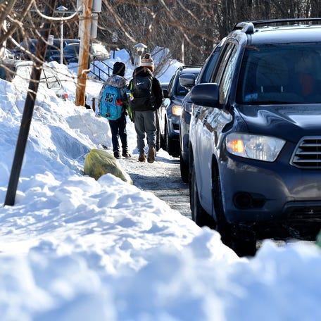 Students walking to West Tatnuck Elementary School squeezes through a snow bank and stopped cars at a section of road lacking a sidewalk.