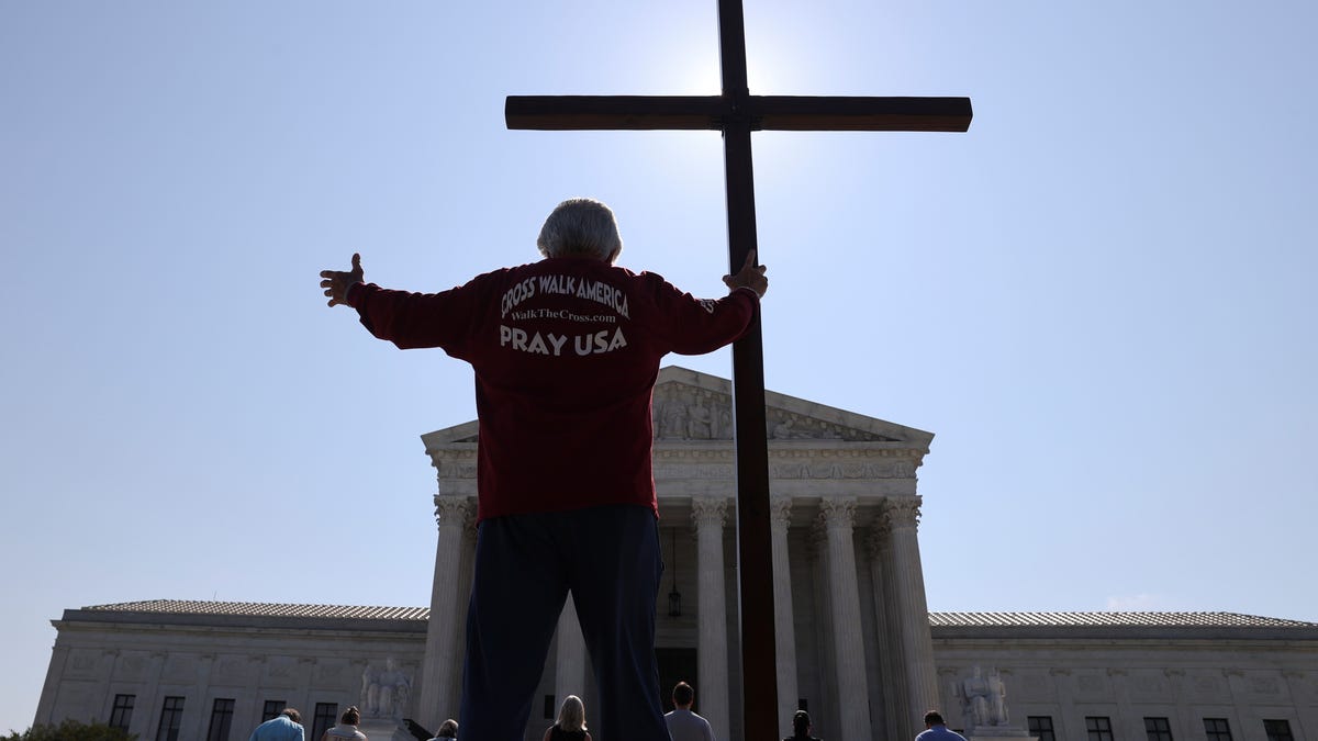 A demonstrator holds a large cross outside the U.S. Supreme Court on July 8, 2020, as the court ruled that religious institutions like churches and schools are shielded from employment discrimination lawsuits.