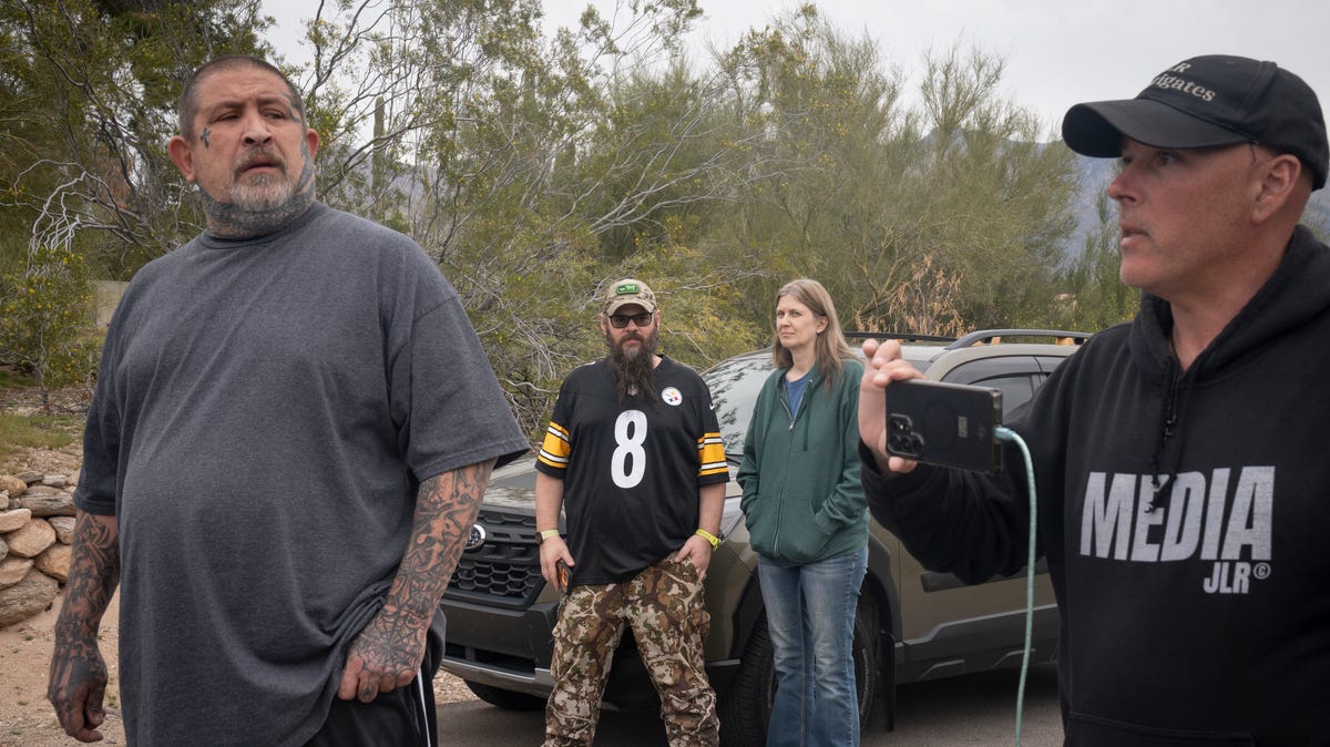 George Schultz (back left) and Crystal Rogers (back right) look on as Jonathan Lee Riches (right, JLR Investigates) live streams outside Annie Guthrie's home in the Catalina Foothills in Tucson, Arizona, on February 16, 2026.