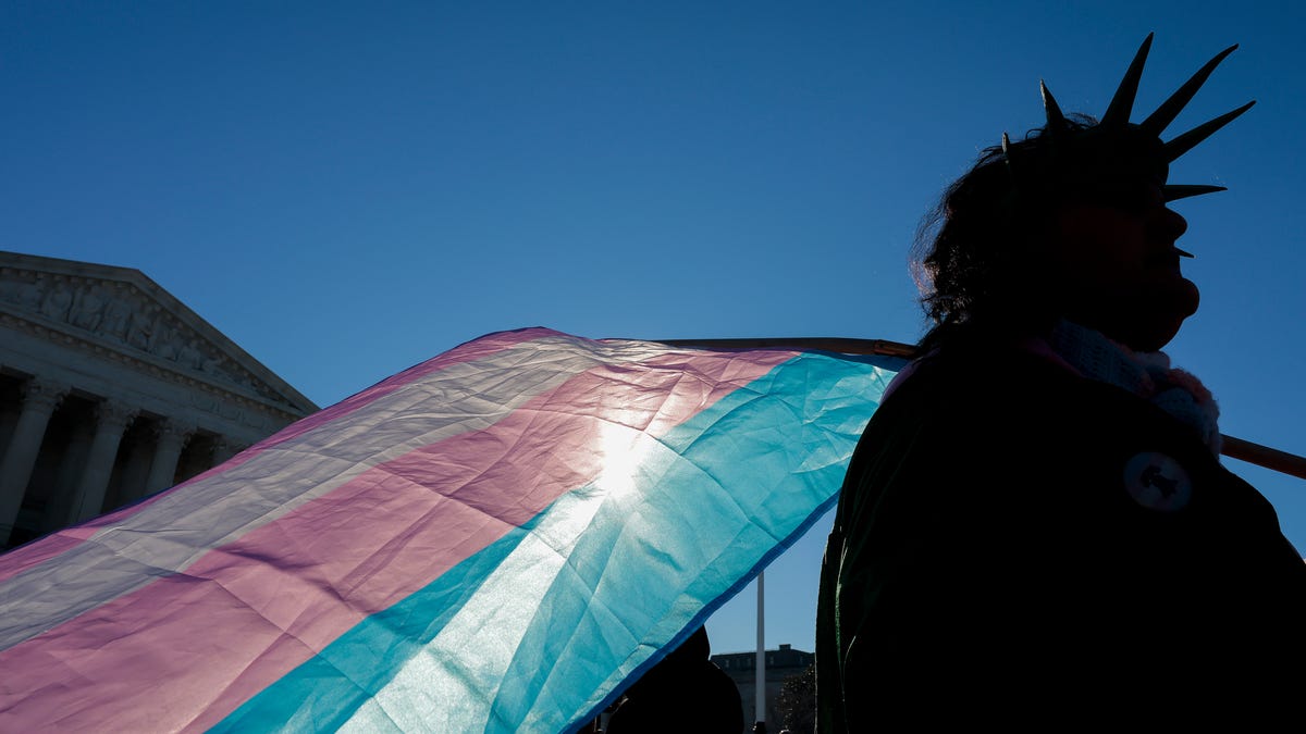 WASHINGTON, DC - JANUARY 13: A protester supporting transgender athletes competing in women's sports holds a transgender pride flag outside the Supreme Court on January 13, 2026 in Washington, DC.