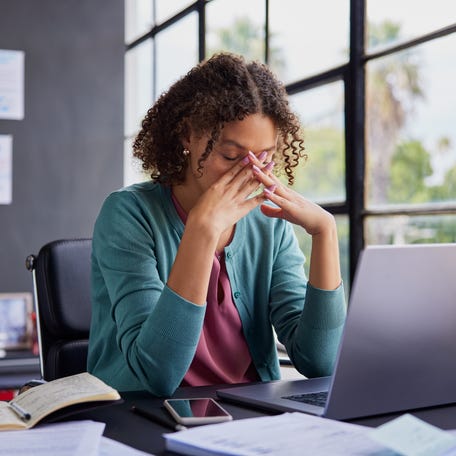 Exhausted businesswoman feeling stressed, holding her head while working on a laptop.