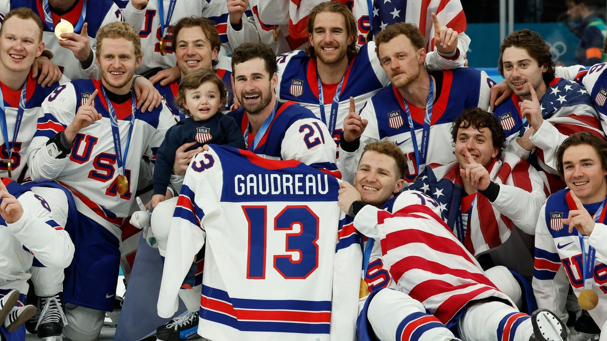 Feb 22, 2026; Milan, Italy; United States players celebrate with a team photo while holding the jersey of Johnny Gaudreau after defeating Canada in the men's ice hockey gold medal game during the Milano Cortina 2026 Olympic Winter Games at Milano Santagiulia Ice Hockey Arena. Mandatory Credit: Geoff Burke-Imagn Images
