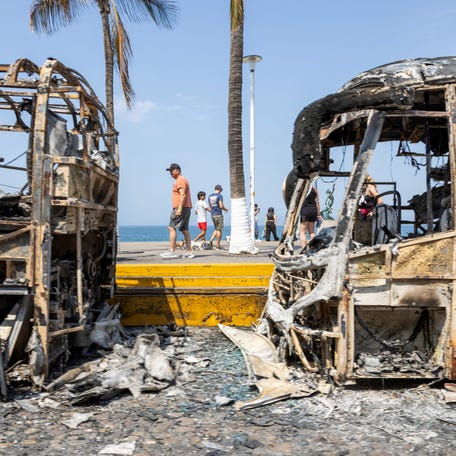 Tourists walk past the burnt wreckage of buses after a series of blockades and attacks by organized crime following a military operation in which cartel boss Nemesio Oseguera, 'El Mencho,' was killed in the state of Jalisco, in Puerto Vallarta, Mexico, February 23, 2026. REUTERS/Alfonso Lepe TPX IMAGES OF THE DAY