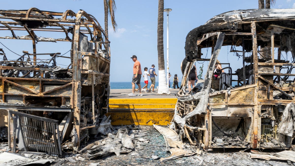 Tourists walk past the burnt wreckage of buses after a series of blockades and attacks by organized crime following a military operation in which cartel boss Nemesio Oseguera, 'El Mencho,' was killed in the state of Jalisco, in Puerto Vallarta, Mexico, February 23, 2026. REUTERS/Alfonso Lepe TPX IMAGES OF THE DAY