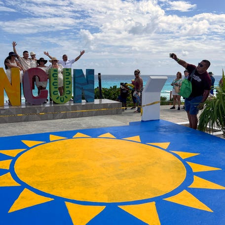 Tourists pose for a picture in front of a Cancun sign in Playa Delfines (Dolphin Beach), at the Hotel Zone of Cancun, Quintana Roo State, Mexico, on November 8, 2022. (Photo by Daniel SLIM / AFP) (Photo by DANIEL SLIM/AFP via Getty Images)