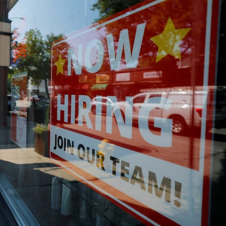 A "Now Hiring" sign hangs in the window of a hair salon in Medford, Massachusetts.