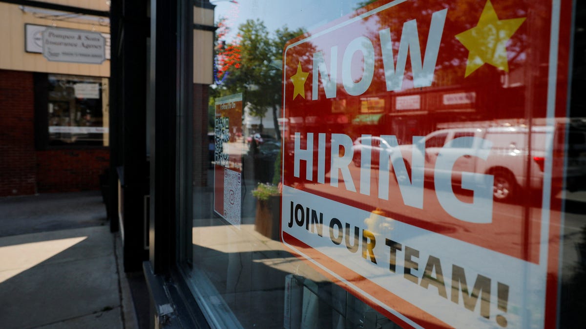 A "Now Hiring" sign hangs in the window of a hair salon in Medford, Massachusetts.