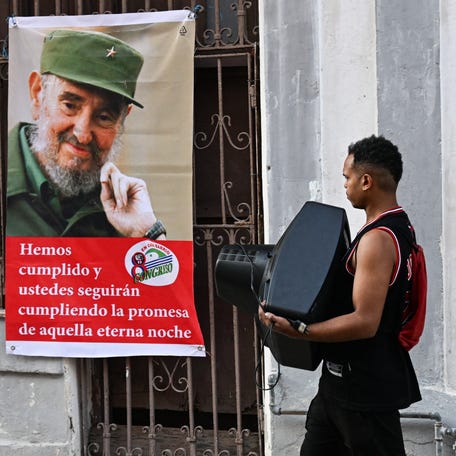 A man carries a television next to a photo of late Cuban leader Fidel Castro in Havana on Feb. 27, 2026. Cuba's communist government lost a key diplomatic supporter, and a vital source of fuel, when the US toppled Venezuelan President Nicolás Maduro.