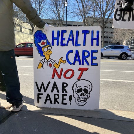 A protester holds a sign reading "Healthcare, not warfare" at a Feb. 28 demonstration, against that morning's US-Israeli military strikes on Iran, in front of Worcester City Hall.