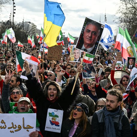 Protesters rally in Paris on March 1, 2026, waving Iranian flags from before the 1979 revolution and portraits of the son of the last shah of Iran and now key opposition figure, Reza Pahlavi.