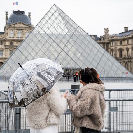 People stand next to fence barriers near the Louvre Pyramid in Paris.