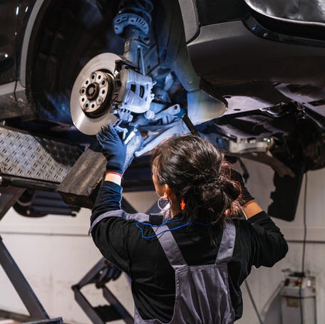 Female mechanic working under a car lifted on a hydraulic lift, inspecting brakes in a professional car repair shop