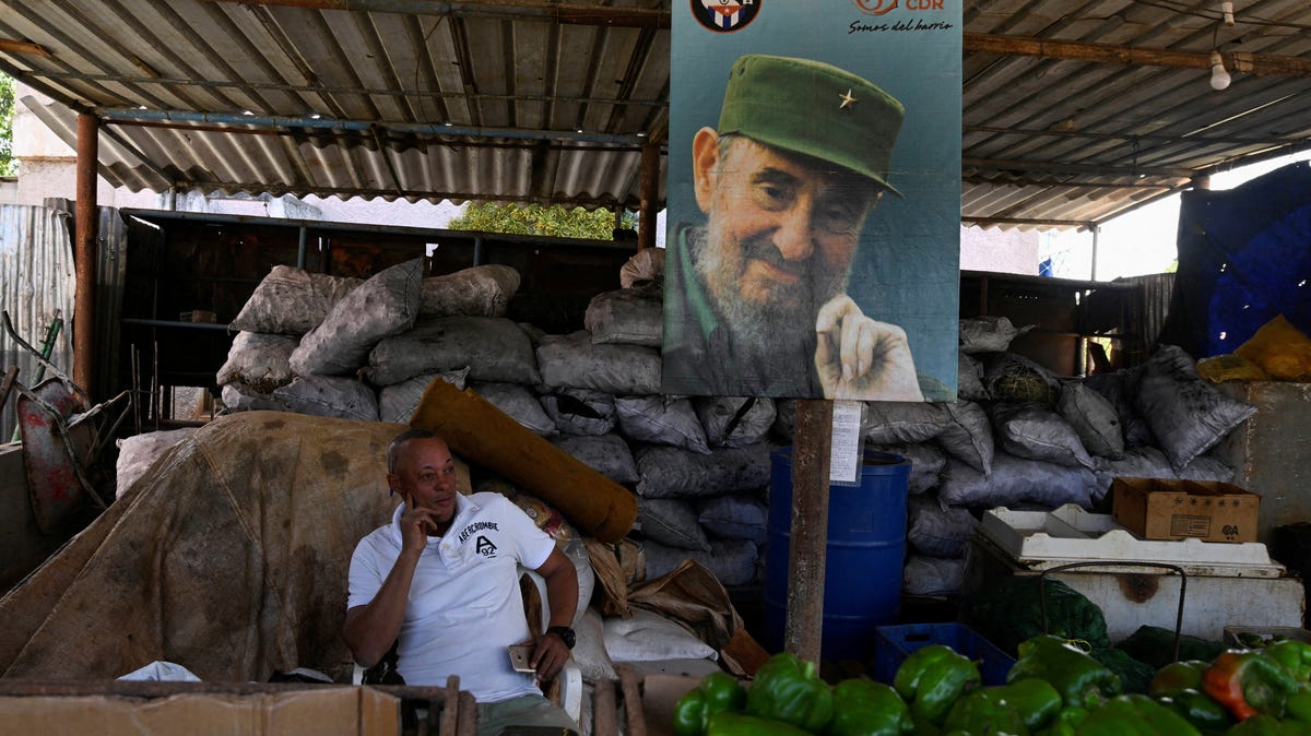 Charcoal seller Ariel Anillo, 52, waits for clients while sitting next to an image of the late Cuban President Fidel Castro in Havana, Cuba, on March 3, 2026.