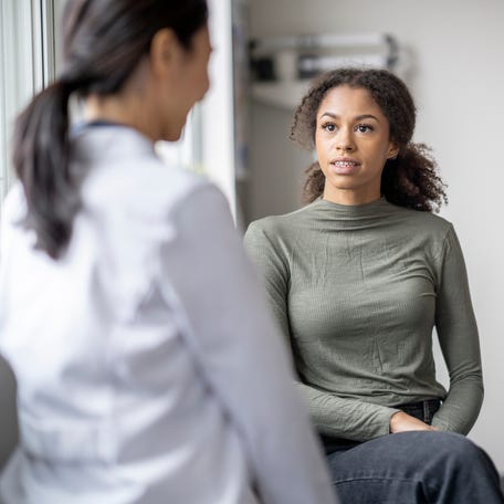 A young female patient sits casually with her doctor as they discuss her health.