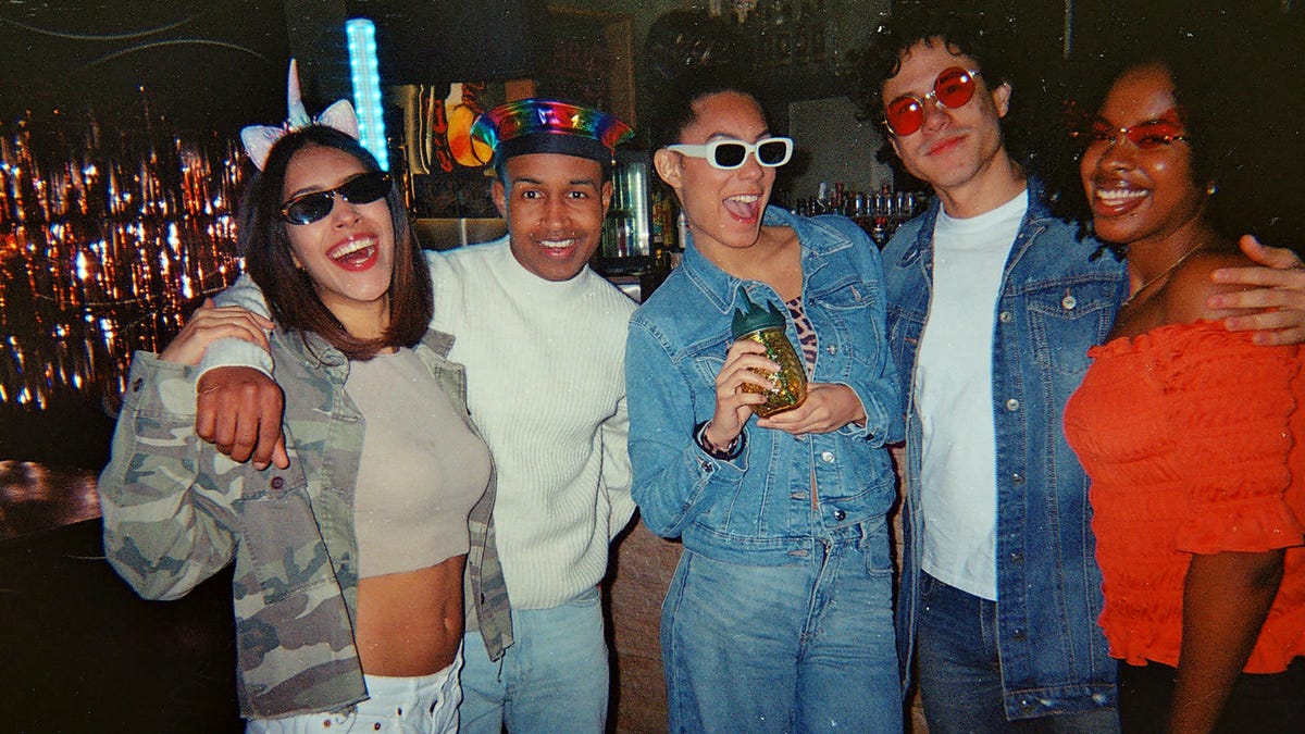 Group of young adults smiling and posing together at a vibrant retro-themed party, candid celebration of friendship, joy, and carefree weekend nightlife energy