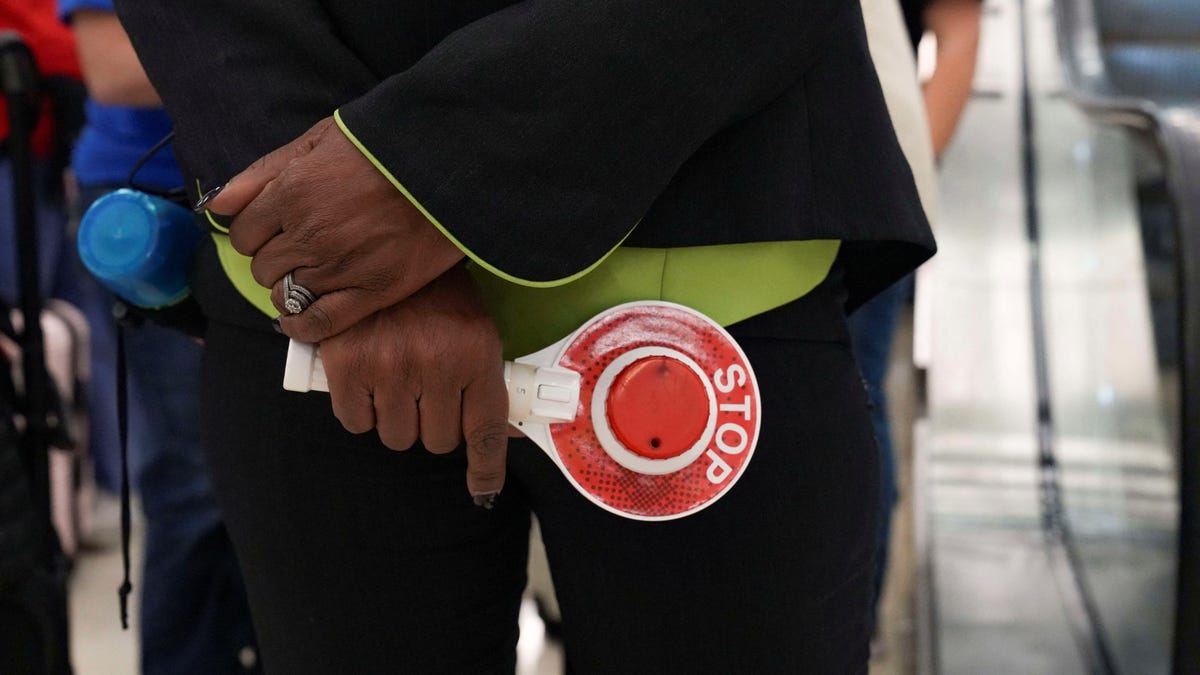 An airport employee holds a stop-and-go light-up sign while directing passengers waiting in long TSA lines amid a partial government shutdown, at Hartsfield-Jackson Atlanta International Airport in Atlanta, Georgia, on March 20, 2026.