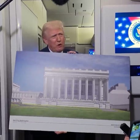 President Donald Trump holds renderings of the planned White House ballroom as he talks with reporters aboard Air Force One en route to Joint Base Andrews, Maryland, on March 29, 2026. 