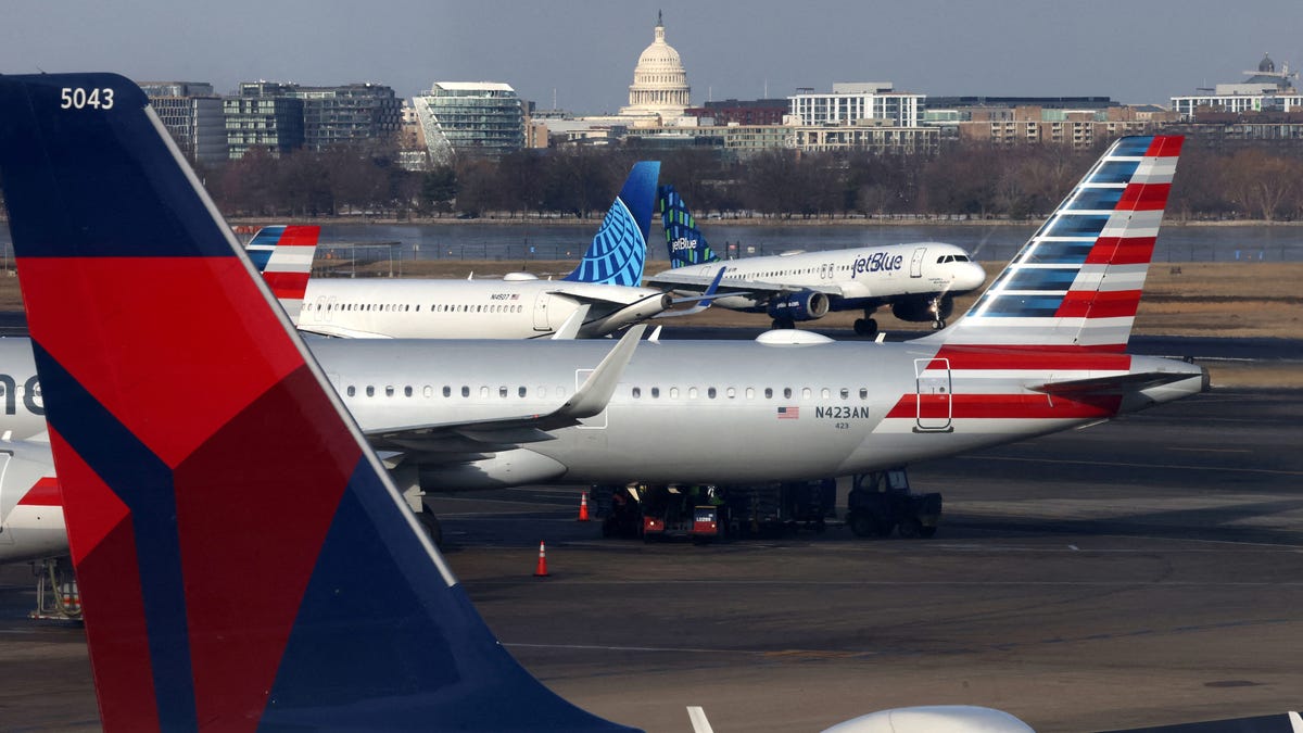 A JetBlue aircraft lands under the DC skyline featuring the U.S. Capitol building, near United Airlines, American Airlines and Delta Airlines aircraft on the tarmac at Ronald Reagan Washington National Airport on January 25, 2025.
