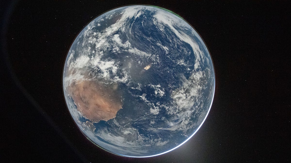 In an image posted by NASA on April 3, 2026, shows a full disk image of Earth, as seen from the Orion capsule. The planet is pale blue, swirling with white clouds and glowing slightly lighter blue in places from reflected light. From the lower left, a large brown landmass is Africa, with the Iberian peninsula twinkling with lights just where the planet curves. In the upper right, aurora glow in a thin green glow, just barely separated from the planet’s surface. Earth is set against
 the black of space.