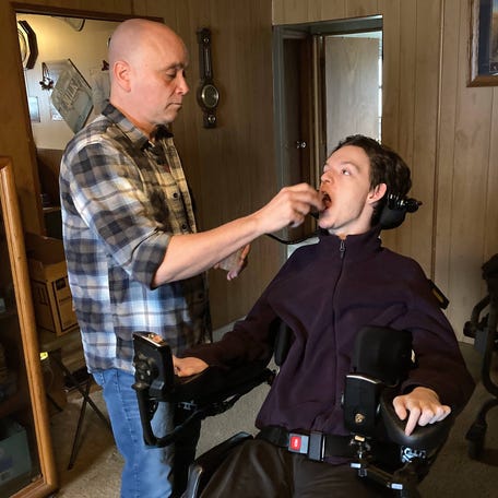 Eliezer Rivera, L.P.N., helps Tyler King take his medicine during a work shift at King's Waterford Township home April 2. King relies on his grandparents and home health nurses including Rivera for his care.
