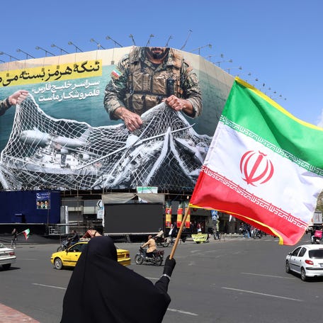 A woman holds Iran's national flag while standing near a billboard at Enqelab Square in Tehran, Iran, on April 5, 2026.