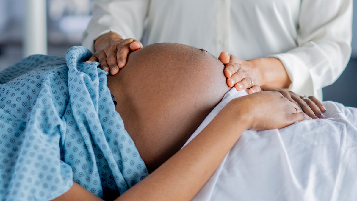 A young pregnant woman of African decent, lays out on an exam table during a prenatal appointment.