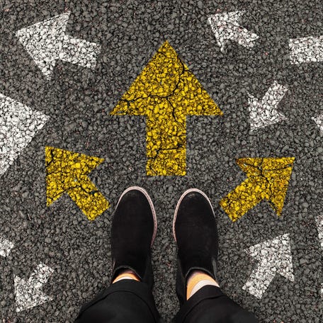Person standing on road with arrow markings pointing in different directions or pathway, decision making concept.