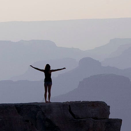 A tourist takes in the view of the layered buttes and canyon walls from a rock outcrop on Mather Point at Grand Canyon National Park in Arizona.