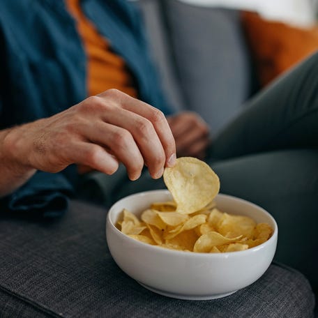 Young unrecognizable young caucasian man at home, sitting on sofa and taking a potato chip from a bowl placed on a sofa