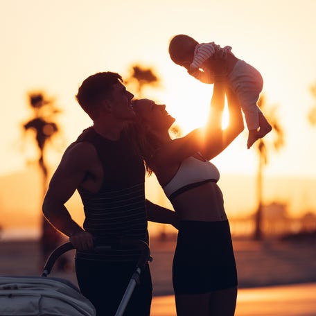 Active family, mother and father, exercising outdoors by the beach in California, running morning jog while pushing her baby pram. Active and healthy lifestyle. Maternity and fitness with baby concept