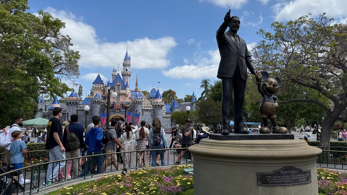 Guests walk past the Partners statue of Walt Disney and Mickey Mouse, heading toward Sleeping Beauty Castle at Disneyland.