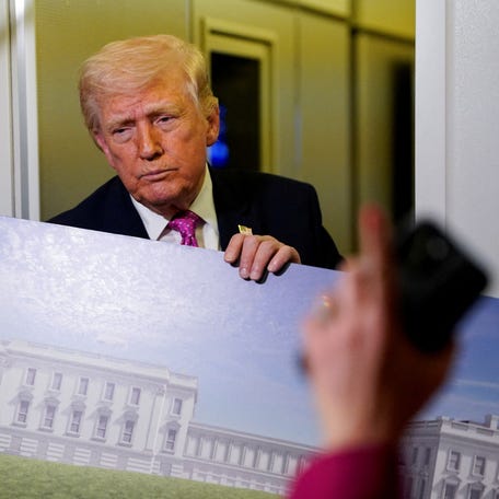 A member of the media raises her hand for a question as President Donald Trump talks while holding up renderings of the planned White House ballroom, aboard Air Force One en route to Joint Base Andrews, Maryland, on March 29, 2026.