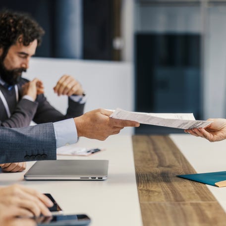 Business professionals exchanging paperwork during a corporate board meeting, symbolizing collaboration, agreement, and legal contract negotiation in an office environment