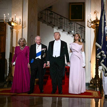 President Donald Trump and first lady Melania Trump escort King Charles III and Queen Camilla to a White House state dinner in Washington, DC, on April 28, 2026. To the right is a painting of Trump reacting as Secret Service agents remove him after an assassination attempt in 2024.