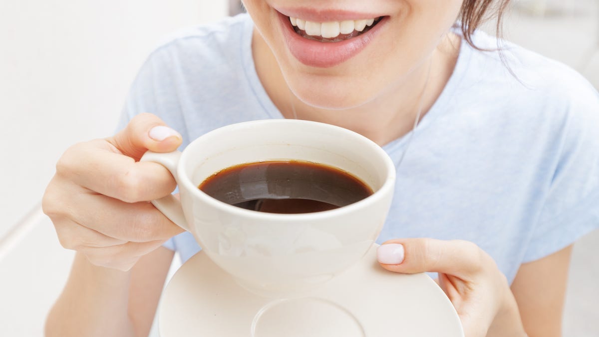 Happy woman drinks a black espresso coffee and smiles.